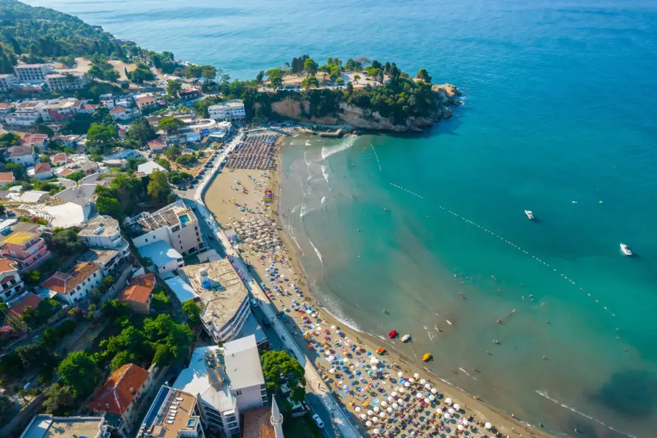 Widok z lotu ptaka na wybrzeże Czarnogóry, z plażą pełną turystów i malowniczymi miasteczkami w tle.
