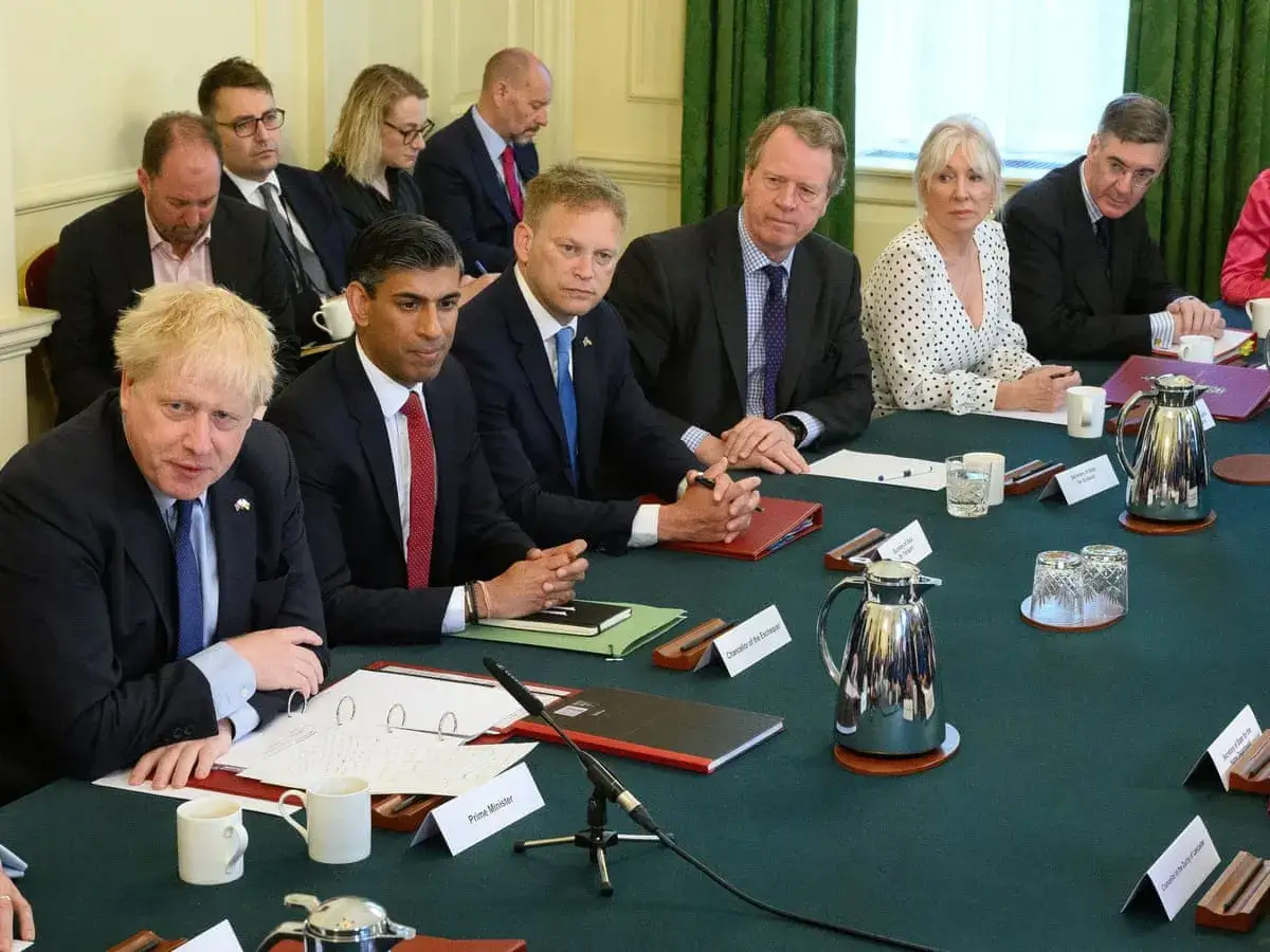 Politicians at a table, embodying public service values, discuss matters of state. Boris Johnson and Rishi Sunak are among those present.