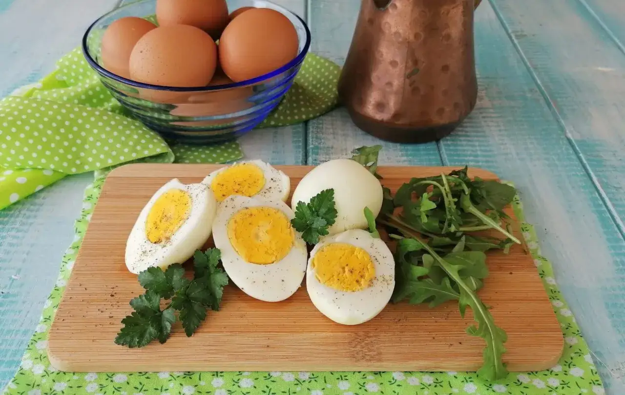 Uova sode in friggitrice ad aria, tagliate a met&agrave;, con un ciuffo di prezzemolo e rucola su un tagliere di legno.