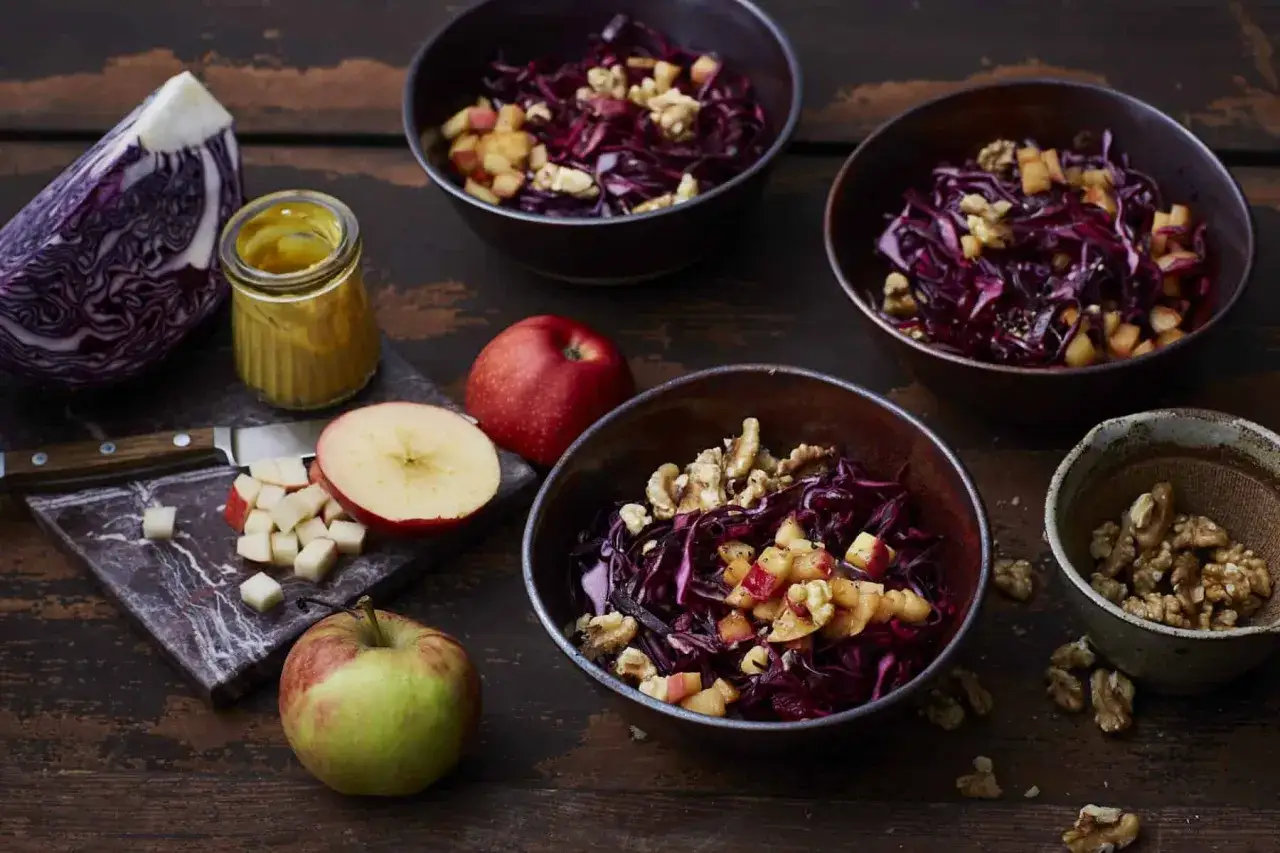 Sch&uuml;ssel mit rotkohlsalat mit apfel und orangen, garniert mit Waln&uuml;ssen. Daneben frische &Auml;pfel und ein Glas Senf.