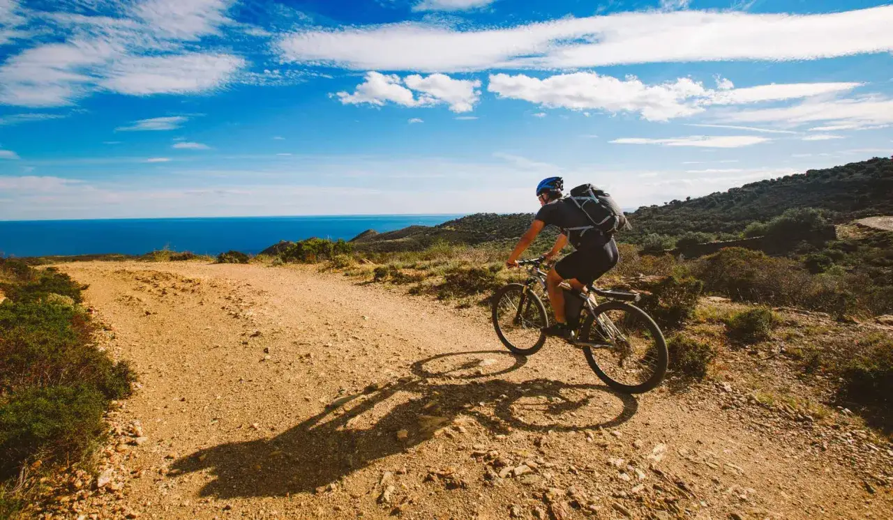 Ciclista pedaleando por sendas ciclables de tierra con el mar azul al fondo.