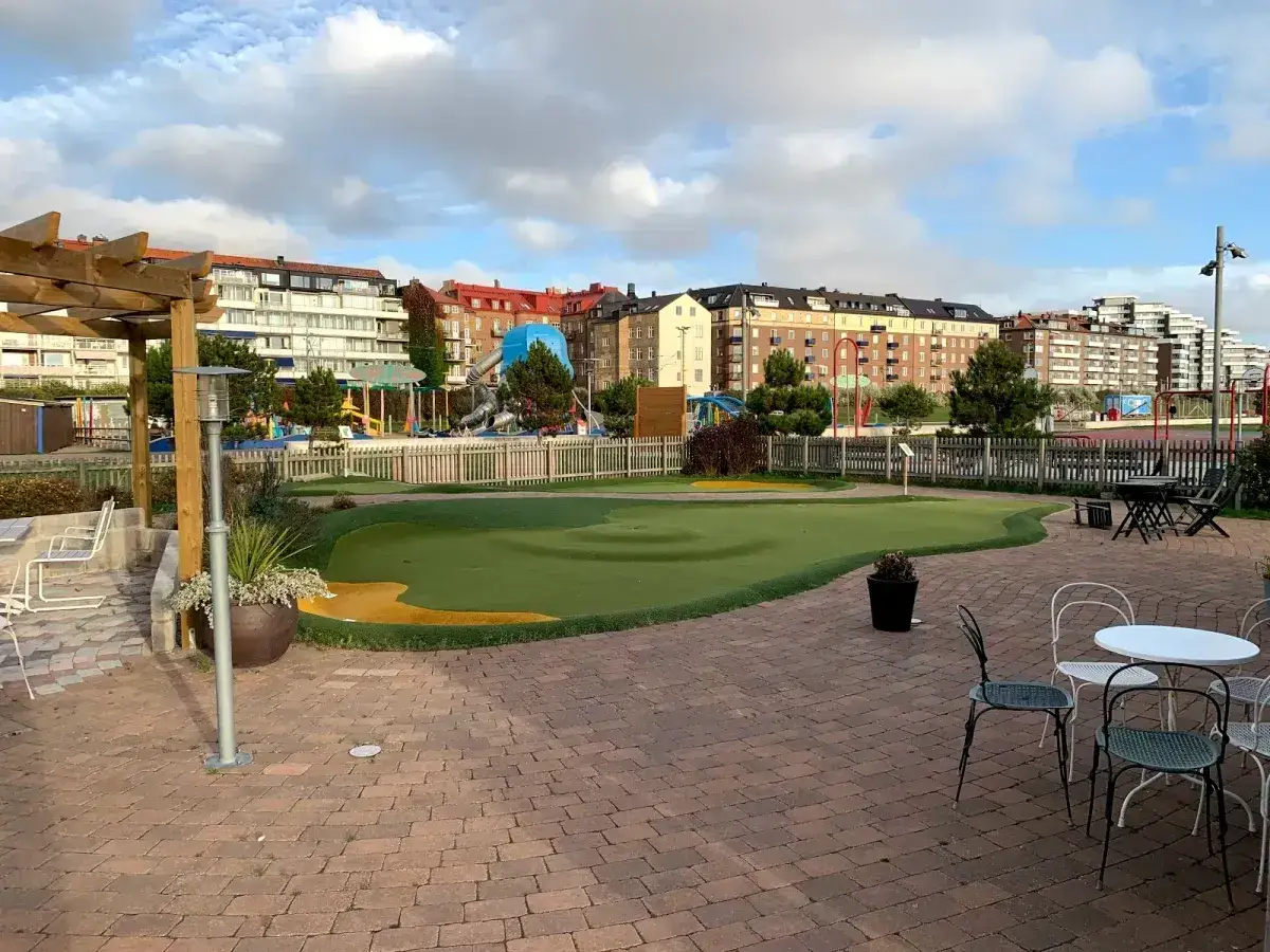 Grönt minigolfområde med lekplats i bakgrunden, en del av minigolf Helsingborg.