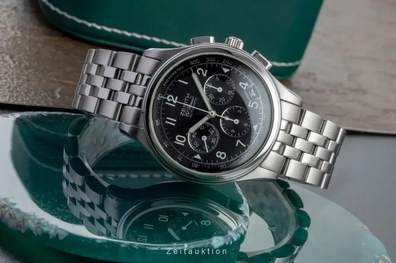Orologio cronografo Zenith El Primero con quadrante nero e cinturino in acciaio, riflesso su una superficie verde.