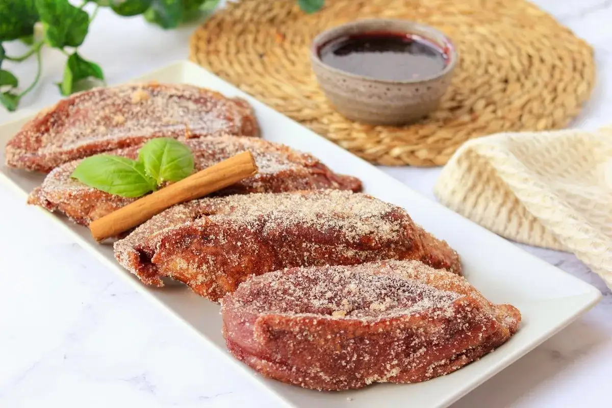 Torrijas de vino espolvoreadas con az&uacute;car y canela, decoradas con una hoja verde y una rama de canela.