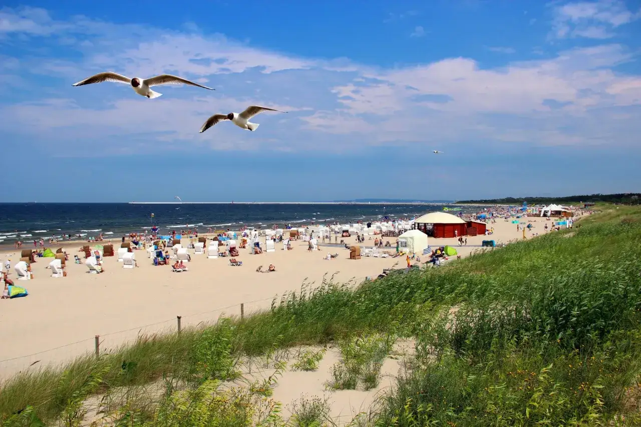 Swinoujscie atrakcje: plaża pełna ludzi, mewy szybujące nad Bałtykiem, słońce i wakacyjny gwar.