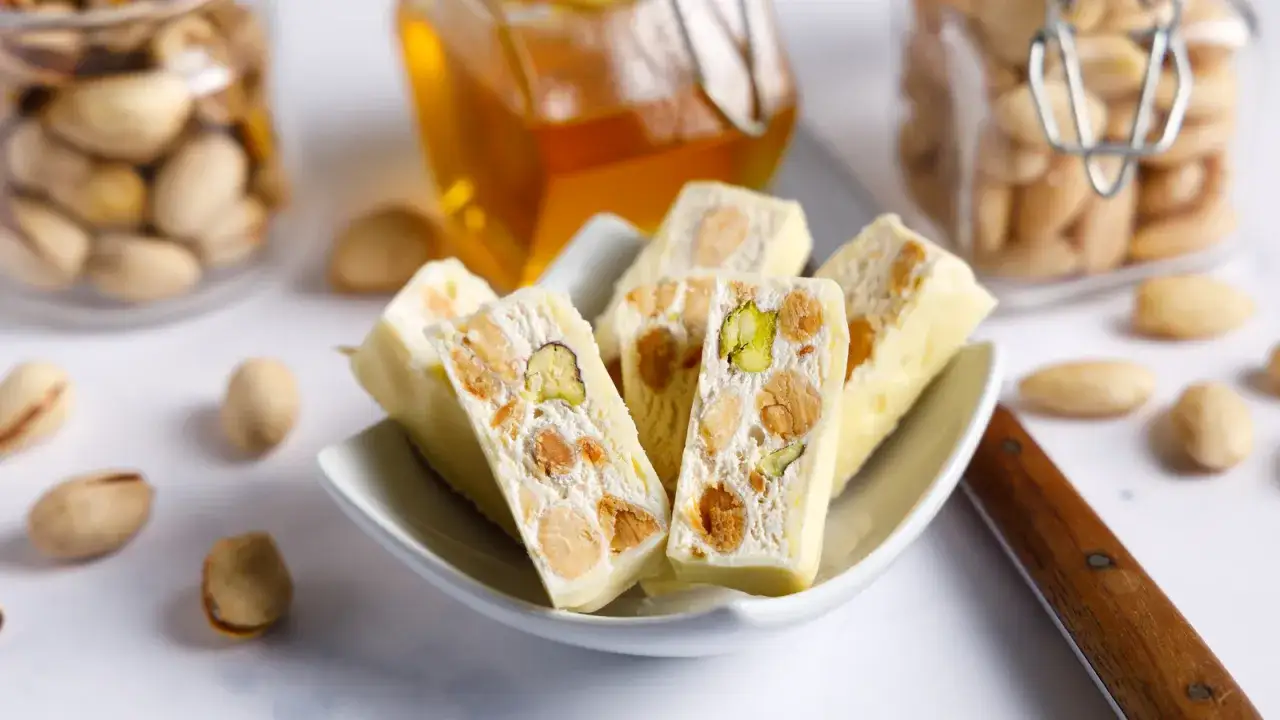 Wei&szlig;er Nougat mit Pistazien und Mandeln, der zeigt, aus was Nougat besteht: N&uuml;sse, Honig und Zucker.