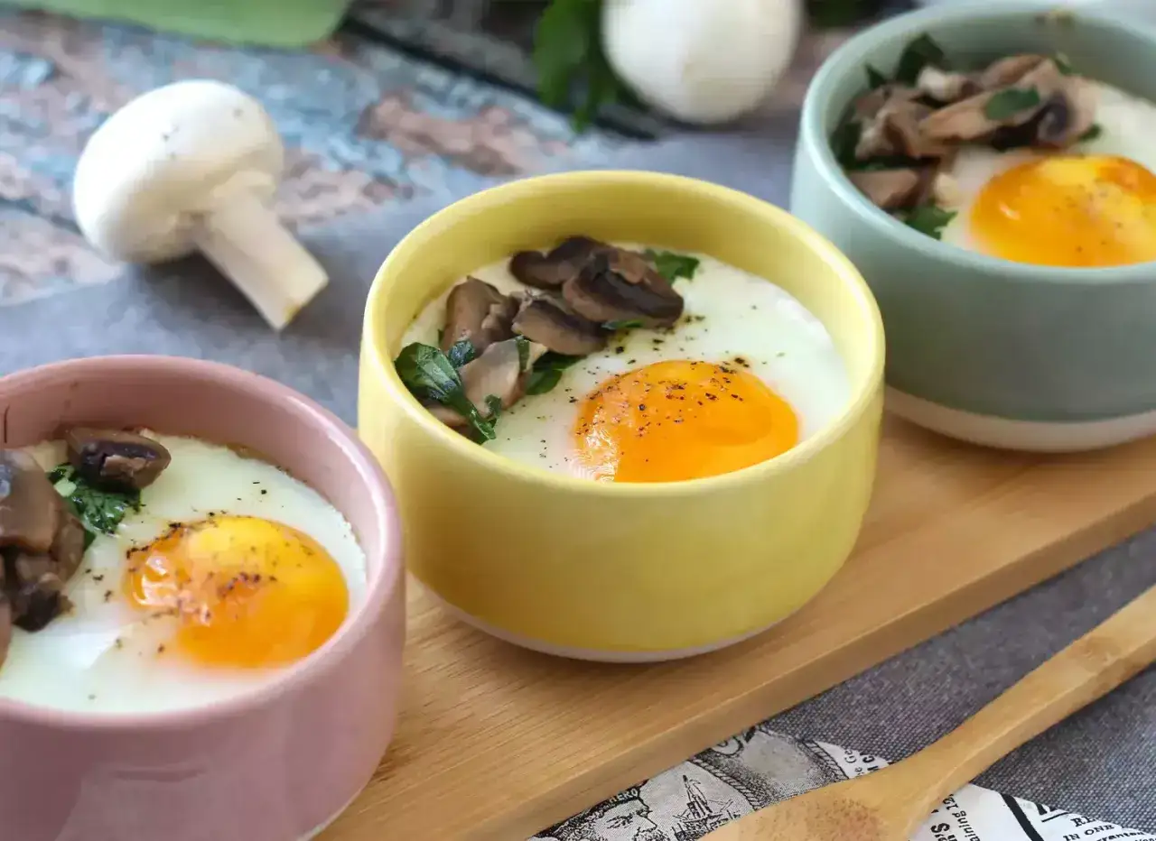 Tres cuencos de colores con huevo al horno, champiñones y espinacas. Un desayuno perfecto y saludable.