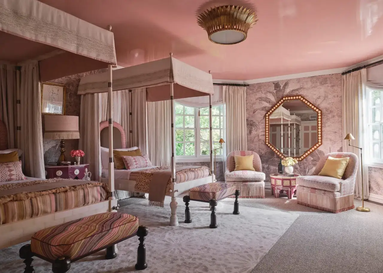 Ein Schlafzimmer in zartem Pink mit zwei Himmelbetten, gemusterten Sitzbänken und zwei Sesseln.