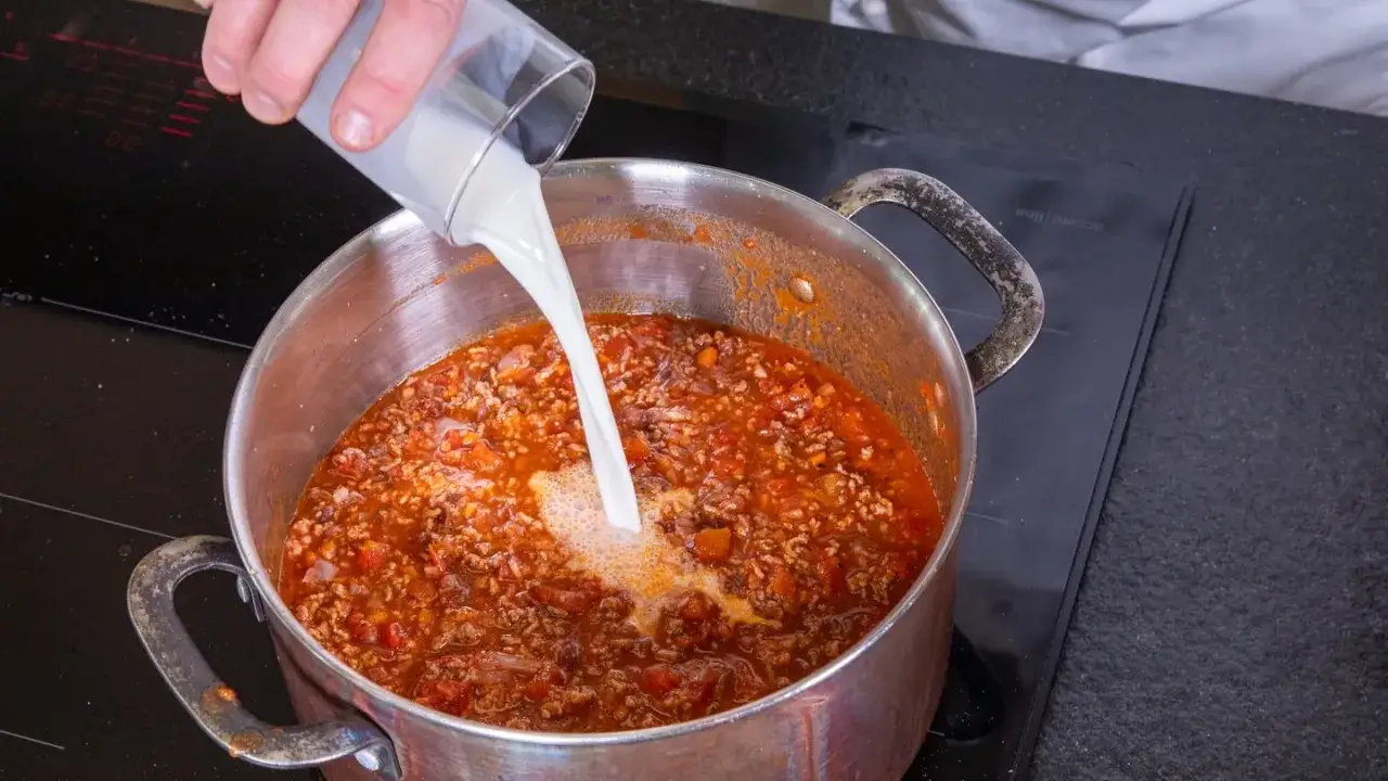Milch wird in einen Topf mit köchelnder Bolognese gegossen, um die Sauce cremiger zu machen.