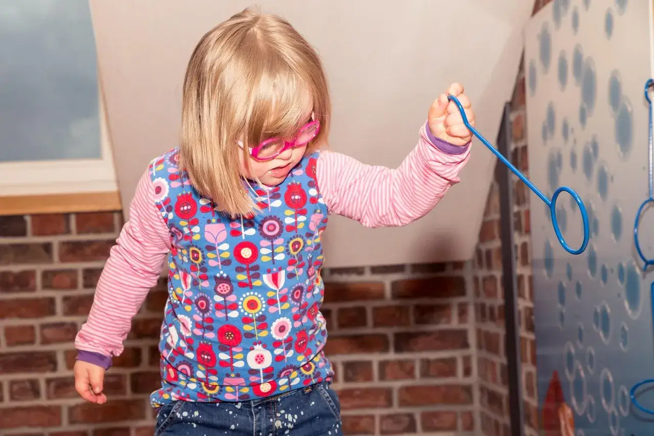 Bambina con sindrome di Down, occhiali rosa, gioca con un cerchio blu. La sua disabilità non le impedisce di divertirsi, superando ogni invalidità.