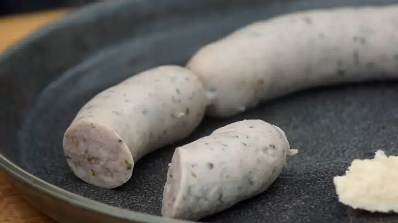 Kiełbasa biała parzona, pokrojona na talerzu, z kawałkiem chrzanu obok.