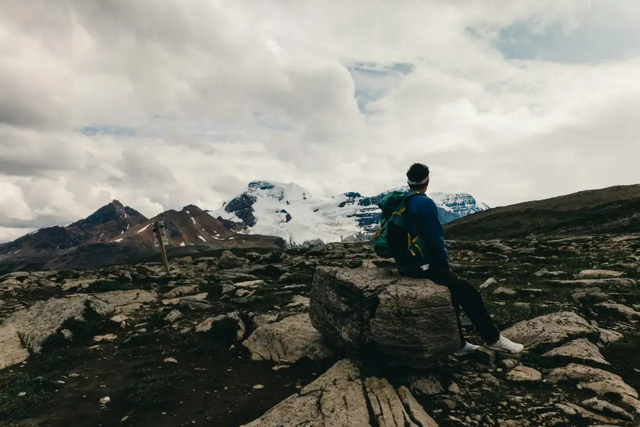 Odpoczynek po trudnym trekkingu. Widok na ośnieżone g&oacute;ry, kamienisty szlak i chmury.