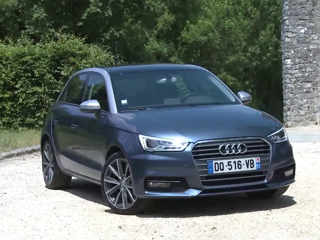 Audi A1 1.0 TFSI 95, une voiture compacte r&eacute;put&eacute;e pour sa fiabilit&eacute;, gar&eacute;e devant un mur de pierre et des arbres.