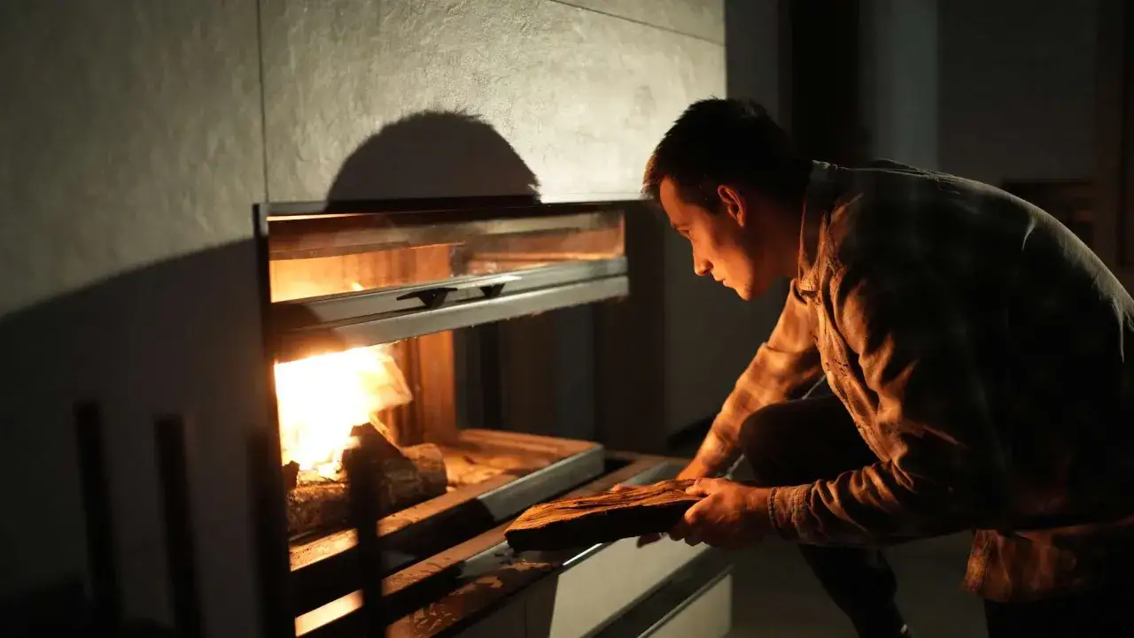 Hombre colocando le&ntilde;a en chimenea moderna para aprovechar su calor.
