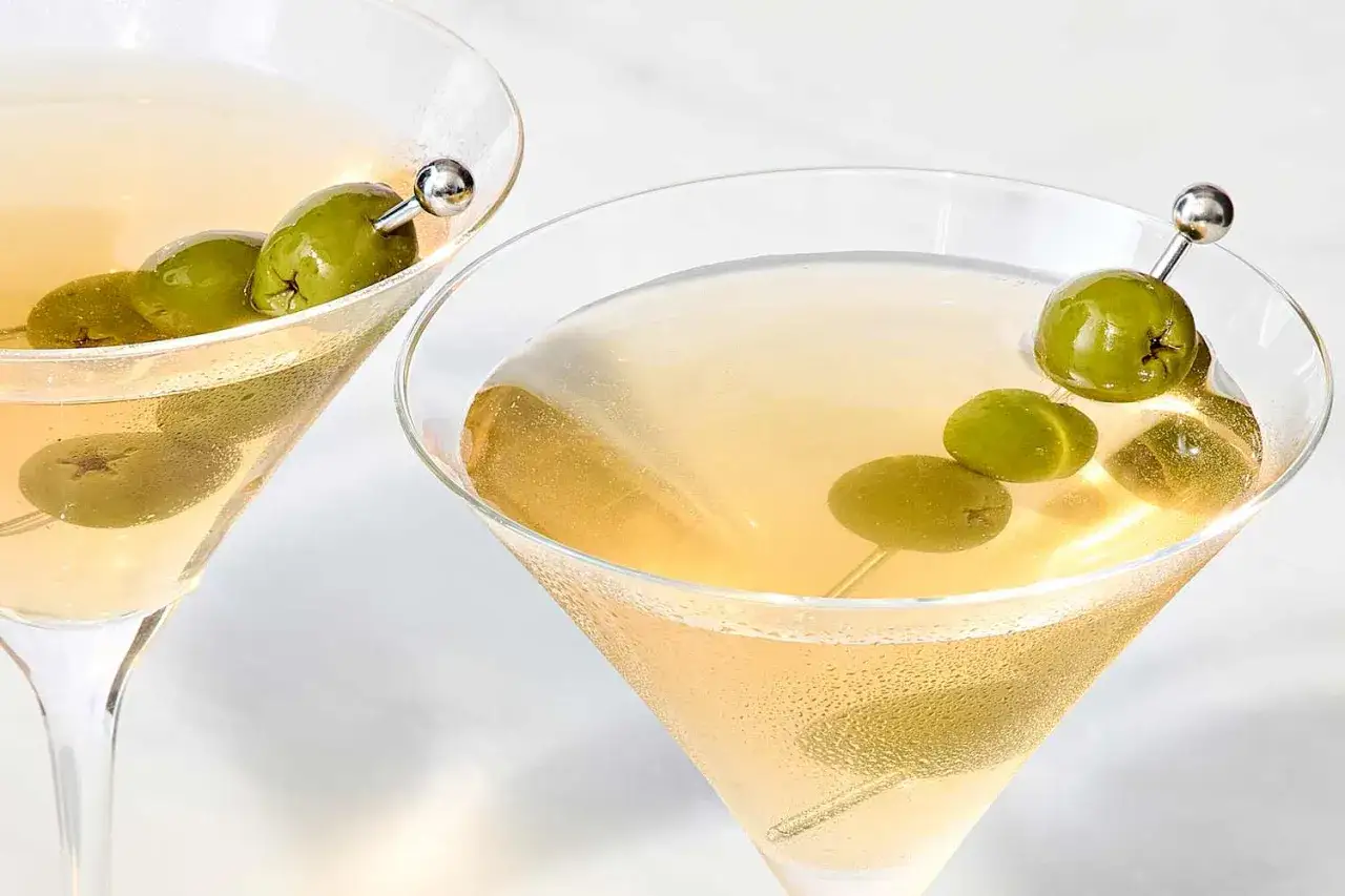 Dwa kieliszki z drinkami, idealne do przepisu na Dirty Martini. Oliwki na wykałaczkach dodają elegancji.