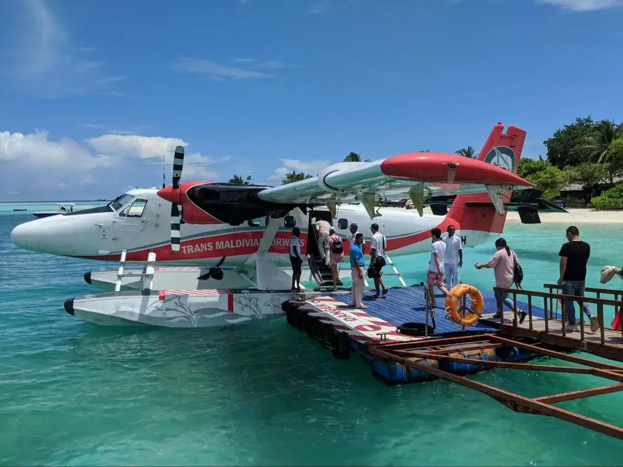 Malediwy loty: pasażerowie wsiadają do wodnosamolotu Trans Maldivian Airways na turkusowej wodzie.