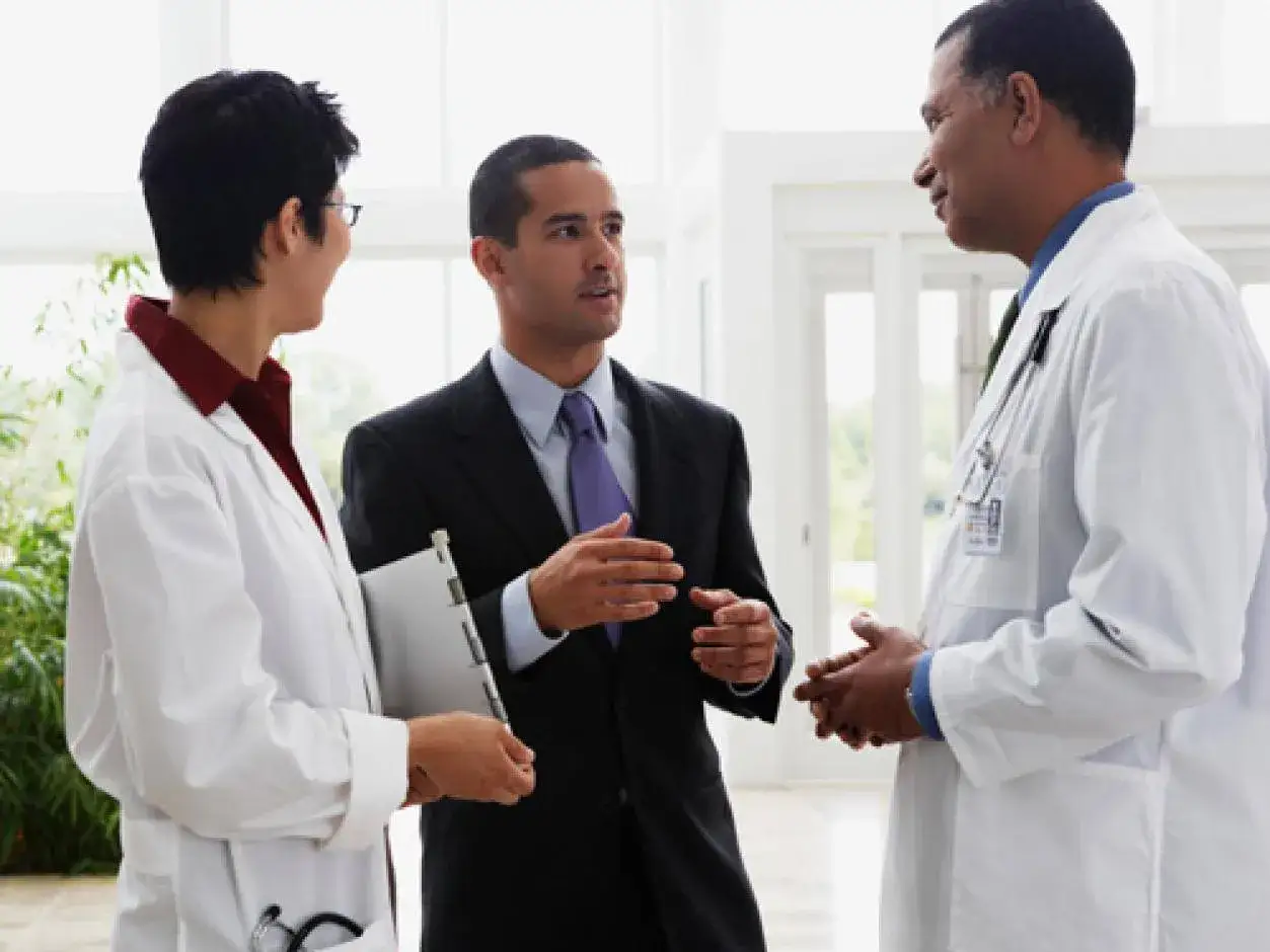 Un uomo in giacca e cravatta parla con due medici. Forse discutono del suo informatore scientifico stipendio.