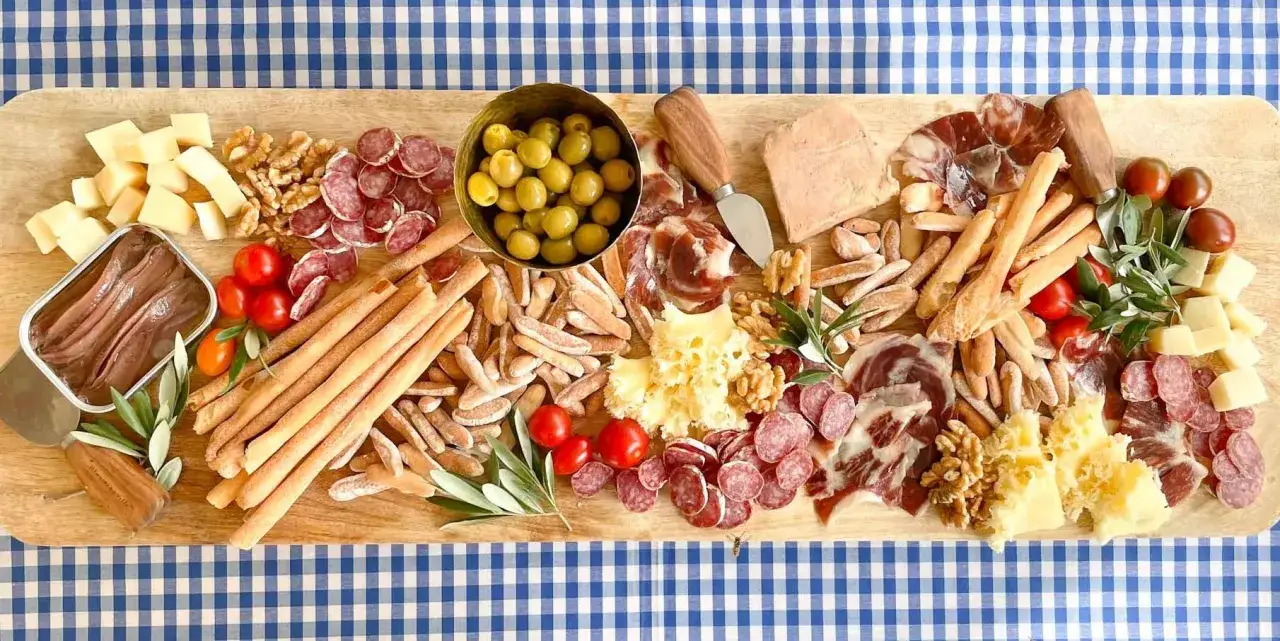 Tabla de quesos y embutidos, ideal para recetas de comidas para cumpleaños adultos. Incluye aceitunas, tomates, frutos secos y anchoas.
