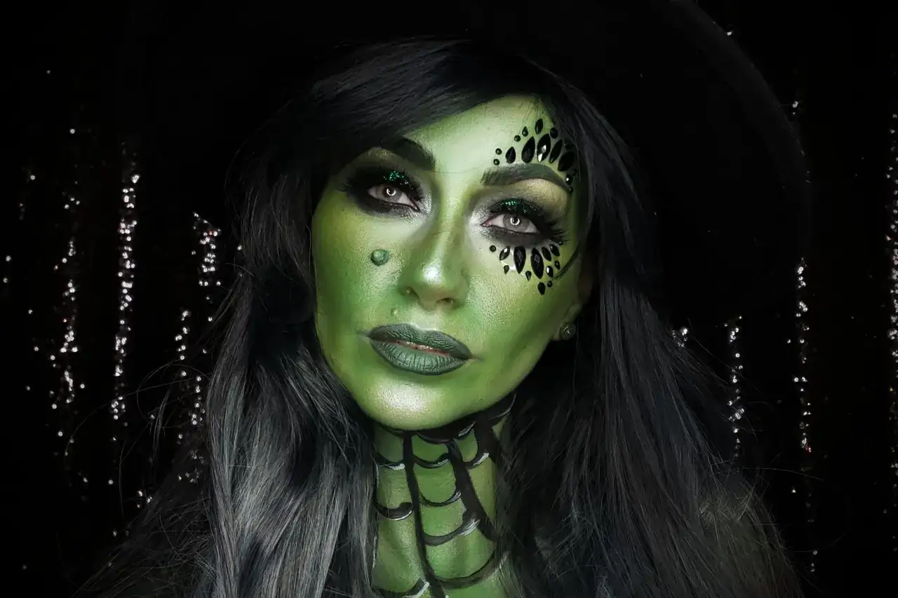 Zielona twarz z czarnymi kryształkami, zielonymi ustami i pajęczyną na szyi. Prosty makijaż czarownicy na Halloween.
