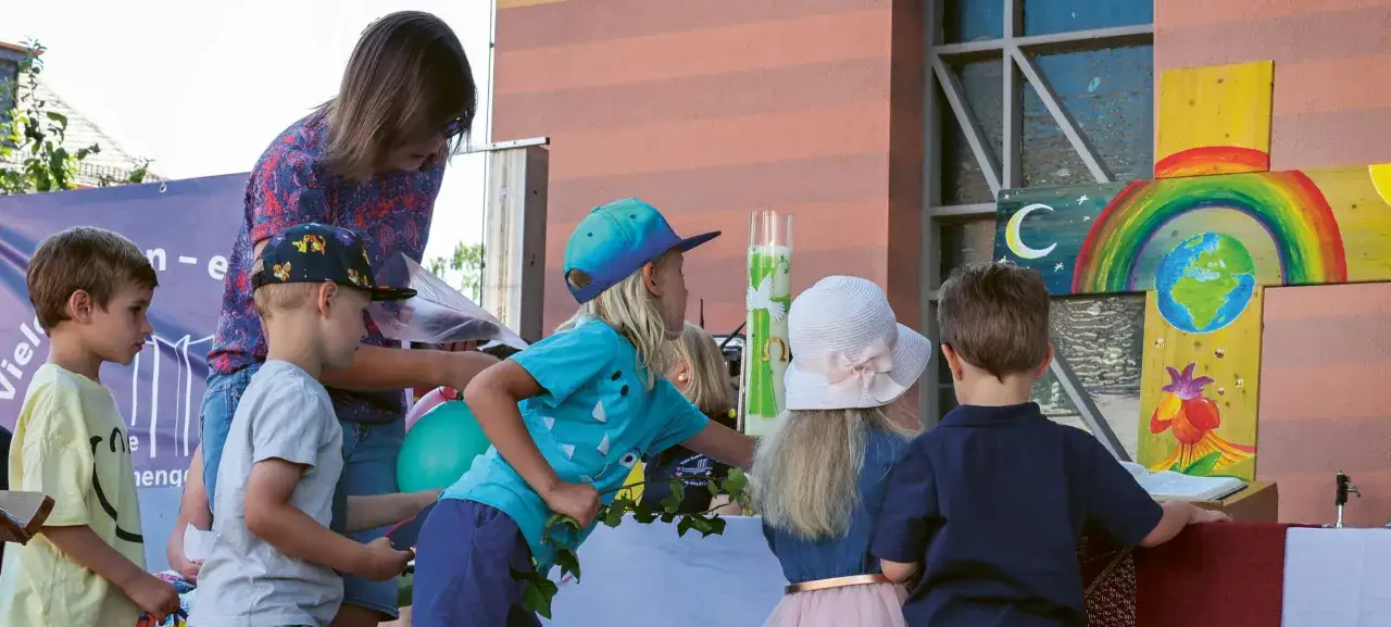 Kinder des evangelischen Kindergartens bestaunen bunte Kreuz-Kunstwerke.
