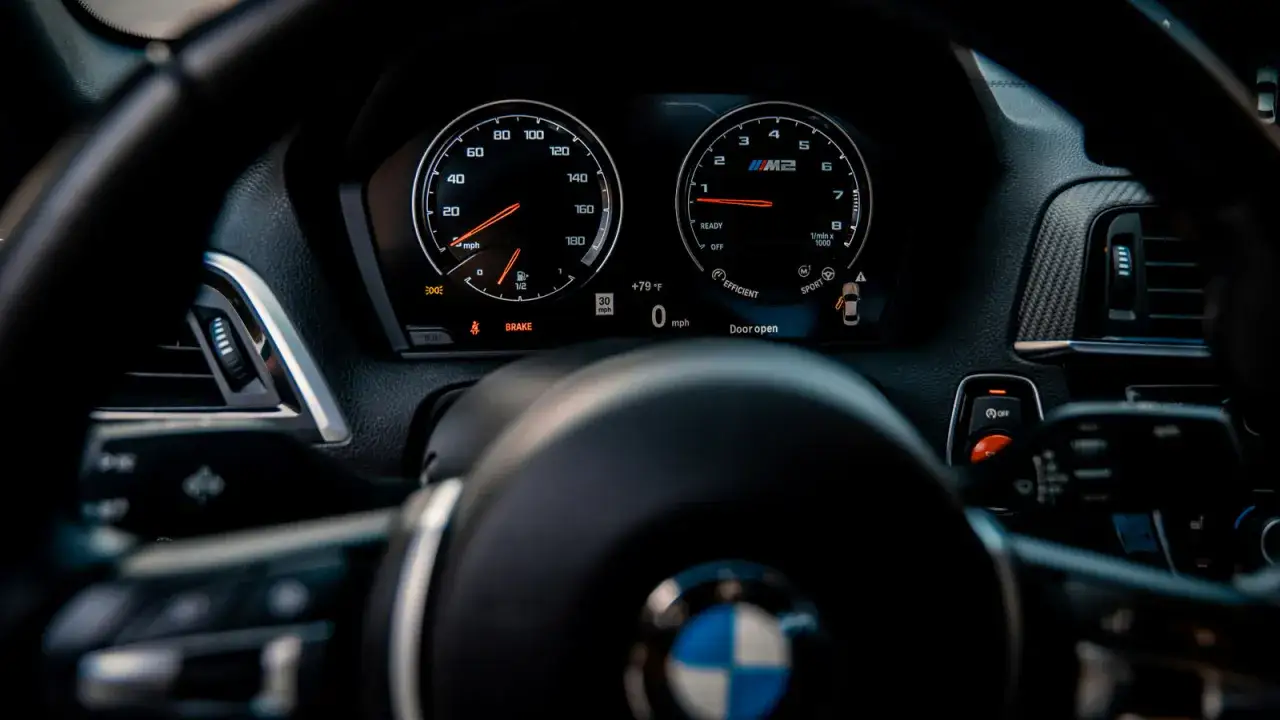 Widok na deskę rozdzielczą BMW M2. Wskaźnik obrotów silnika pokazuje niską wartość, a obok wyświetlacz informuje o otwartych drzwiach.