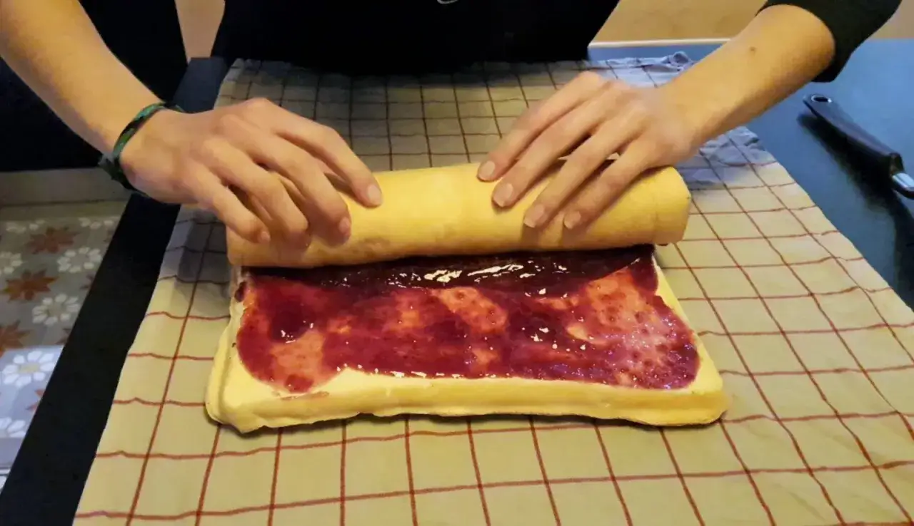 Mains expertes commencent &agrave; rouler un g&acirc;teau garni de confiture de fruits rouges.