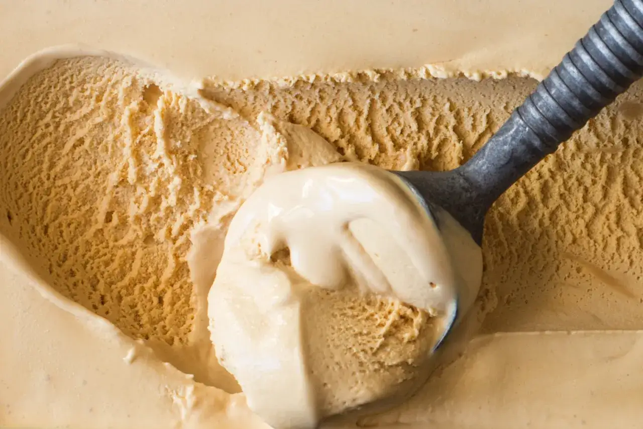 Ein Löffel nimmt eine Kugel cremiges, goldbraunes salted caramel eis auf.