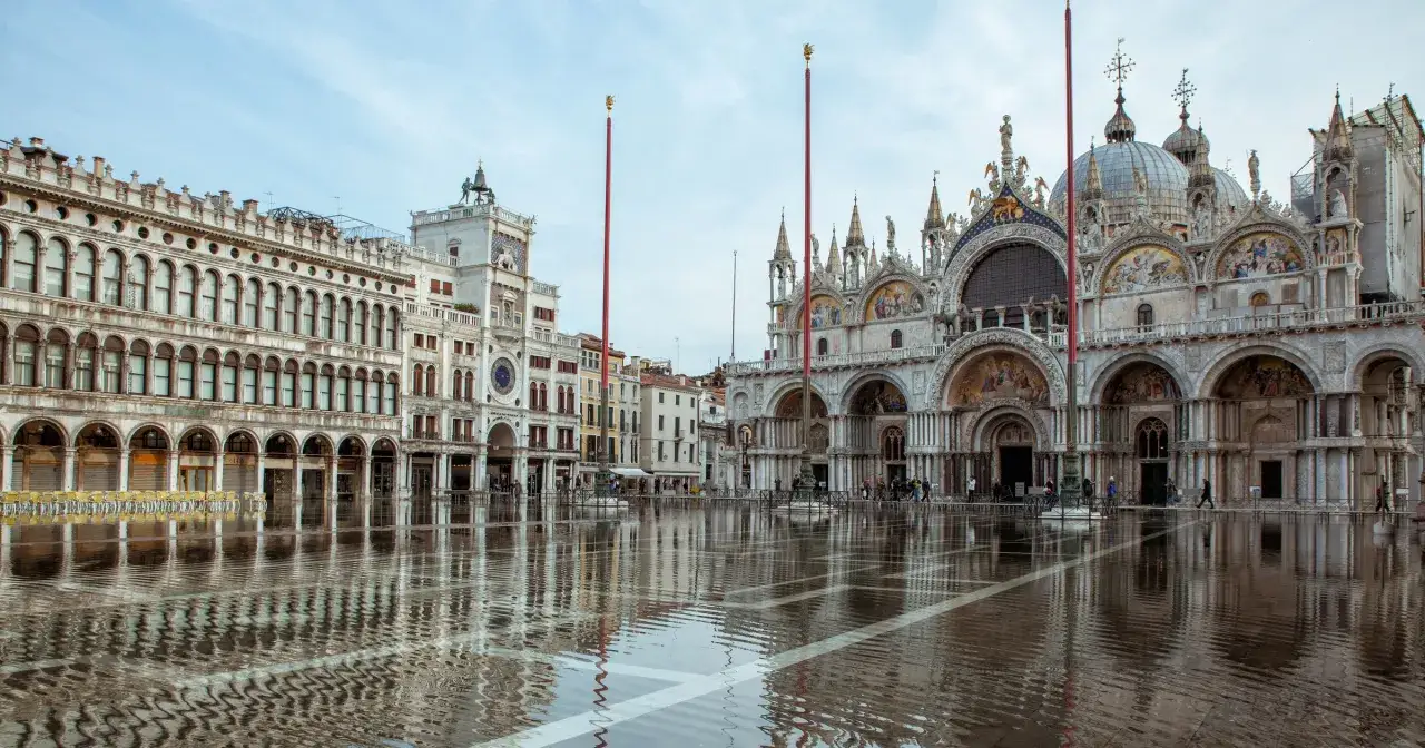 Piazza San Marco w Wenecji zalana wodą, odbijającą wspaniałą bazylikę i wieżę zegarową.