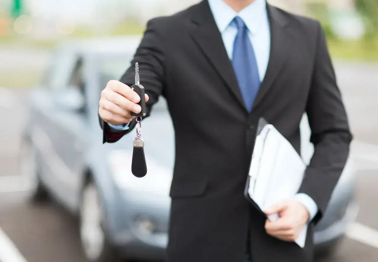 Biznesmen w garniturze oferuje kluczyki do samochodu, symbolizując leasing Peako.