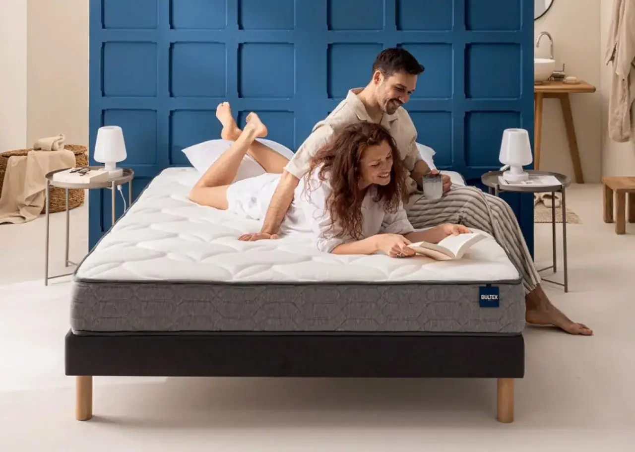 Couple profitant d'un moment de d&eacute;tente sur un matelas 2 places. Elle lit, il boit un caf&eacute;. Confort et intimit&eacute; assur&eacute;s.
