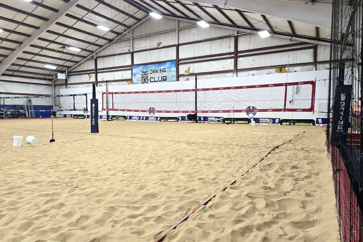 Wnętrze hali do siatkówki plażowej. Piasek, siatka, słupki i tablica z napisem