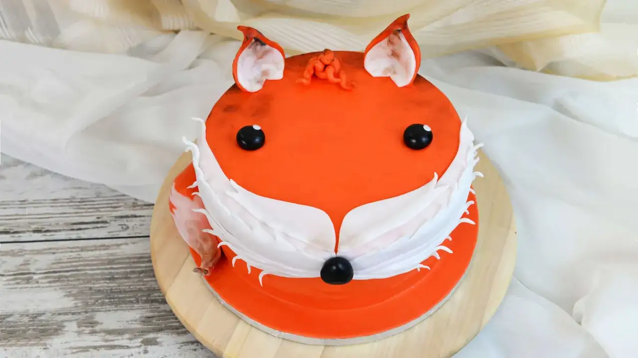 Pomarańczowy tort w kształcie lisa z białym futerkiem i czarnym noskiem. Idealne proste torty dla chłopc&oacute;w na urodziny.