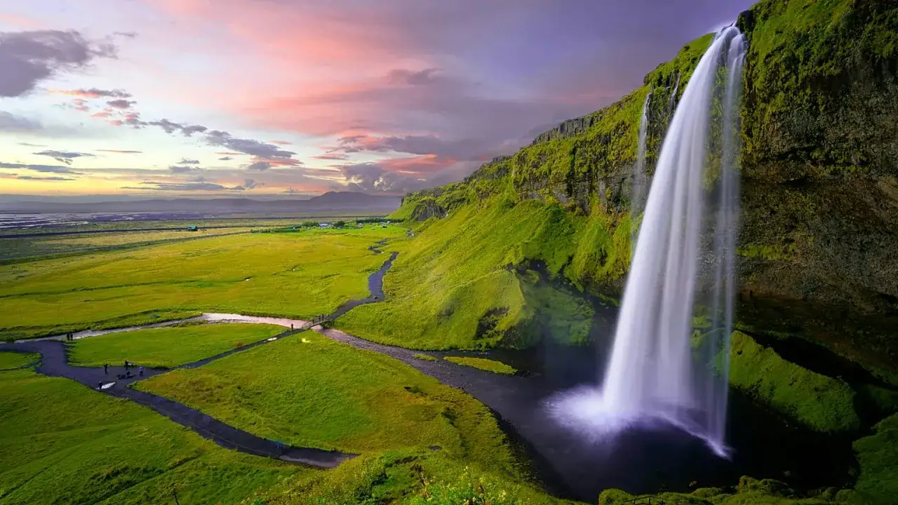 Cascata imponente in un paesaggio verdeggiante, con un cielo rosa al tramonto. Un luogo che evoca la pace e la bellezza dei paesi pi&ugrave; sicuri al mondo.