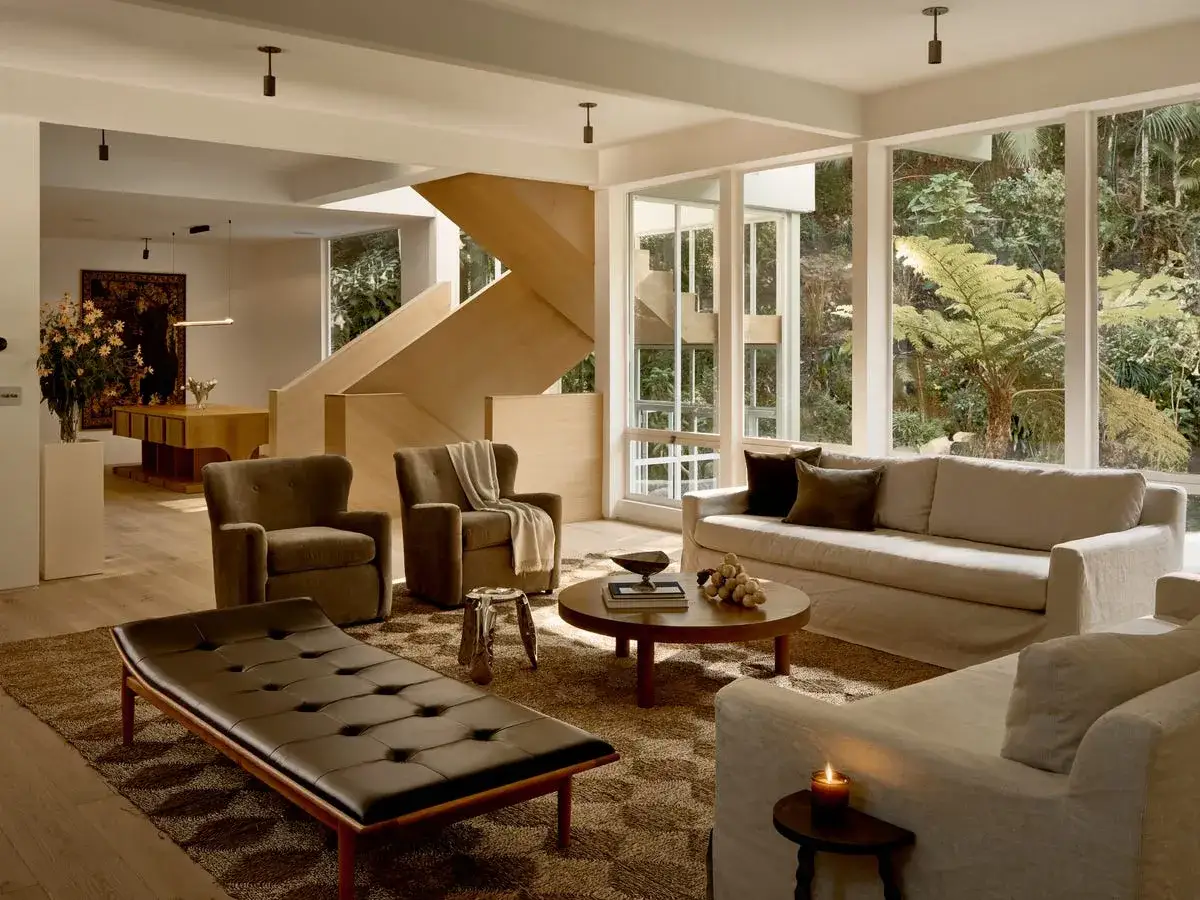 Elegante sal&oacute;n con chaise longue de cuero, sof&aacute;s de lino y escaleras de madera, evocando el interiorismo a&ntilde;os 60.