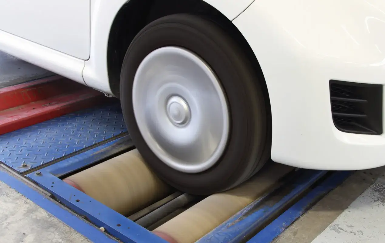 Roue d'une voiture blanche sur un banc de rouleaux, en cours de previsite controle technique.