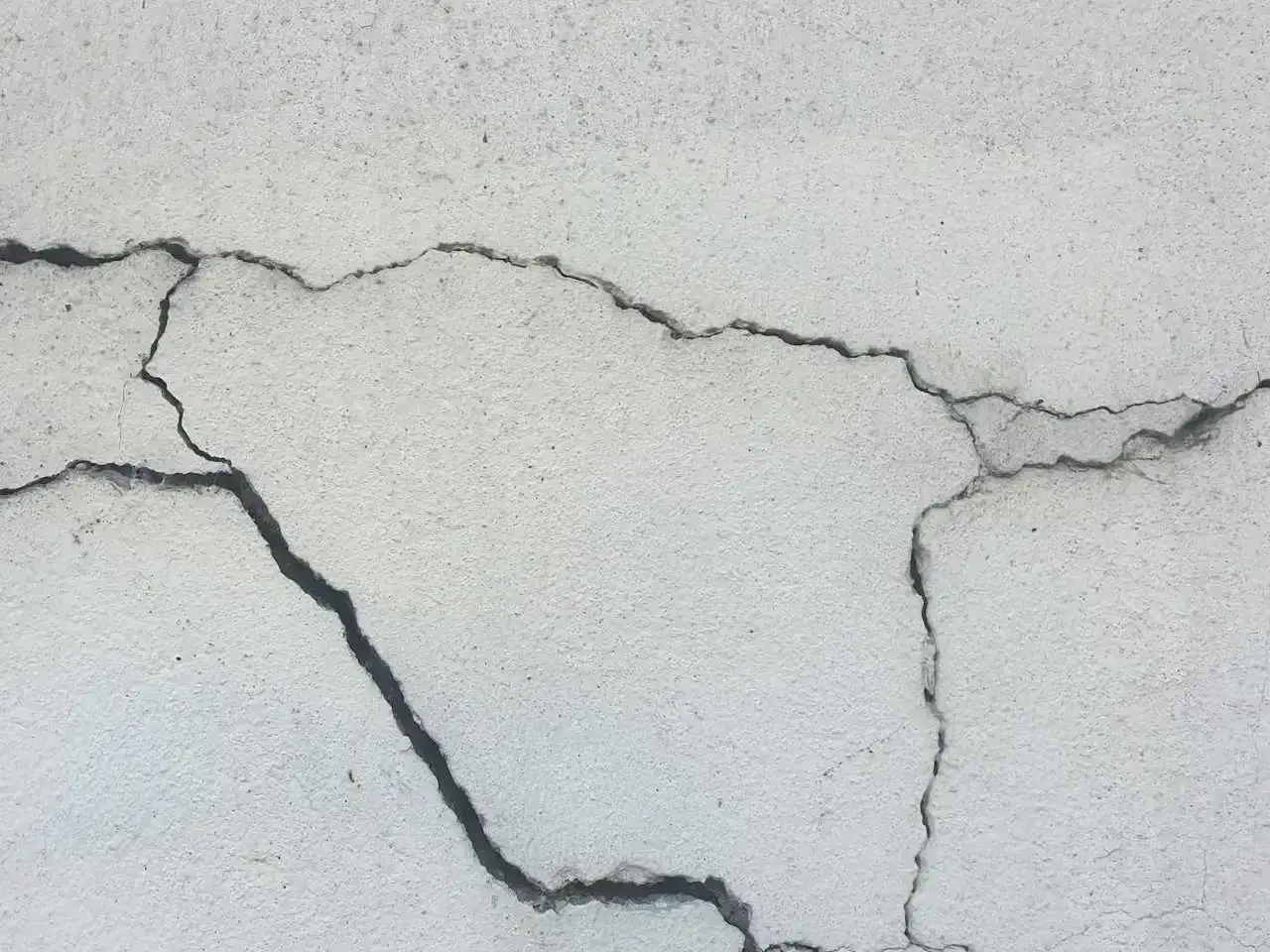 Pęknięcia na jasnej powierzchni betonu, świadczące o procesie karbonatyzacji.