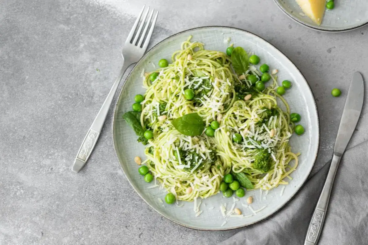 Assiette de tagliatelle de courgette, pois, pignons et parmesan râpé, garnie de feuilles de basilic frais.