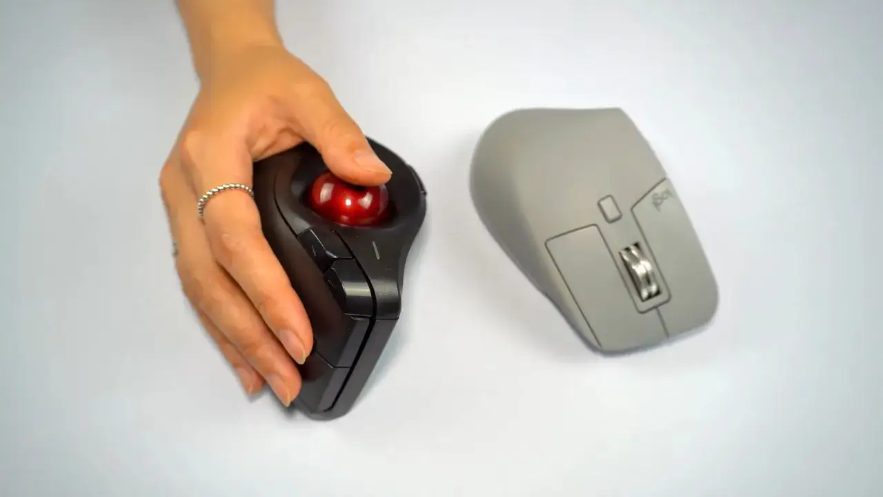 Main gauche, une main utilise une souris trackball noire. À droite, une souris grise. Quelle souris ergonomique choisir pour votre confort ?