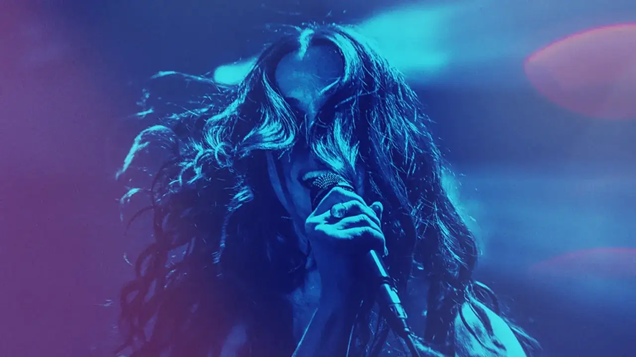 Intensywny alanis morissette koncert. Wokalistka z burzą włosów śpiewa do mikrofonu w niebieskim świetle.
