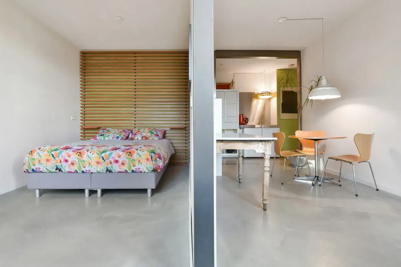 Aménagement d'un studio 30m2 en 2 pièces : chambre avec lit fleuri et espace cuisine/salle à manger.