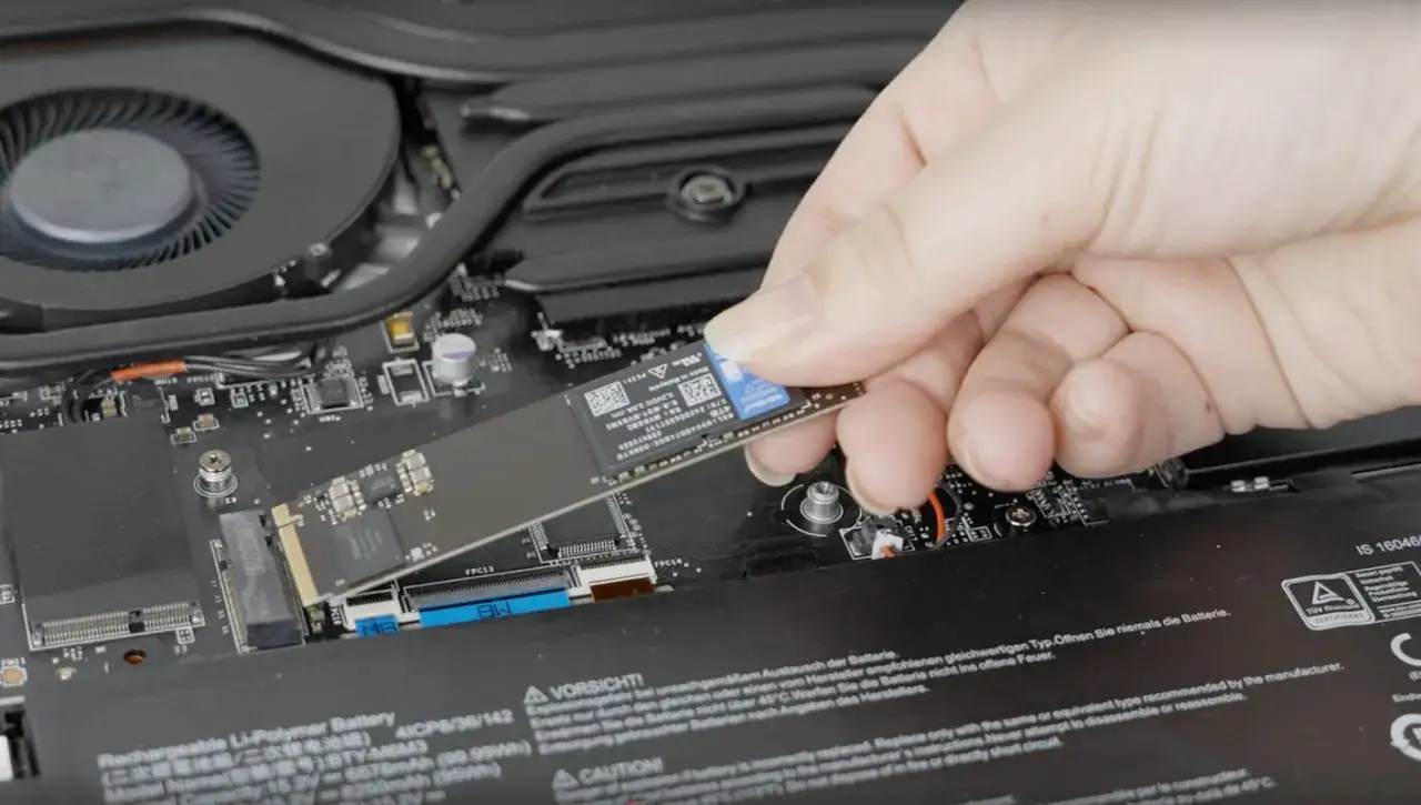 Dłoń montuje dysk SSD M.2 do płyty głównej laptopa. Zobacz, jak zamontować dysk SSD.