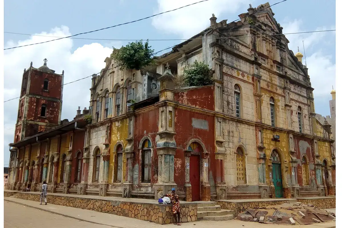 Vieux b&acirc;timent color&eacute; &agrave; Porto-Novo, avec une tour carr&eacute;e et des plantes grimpantes.