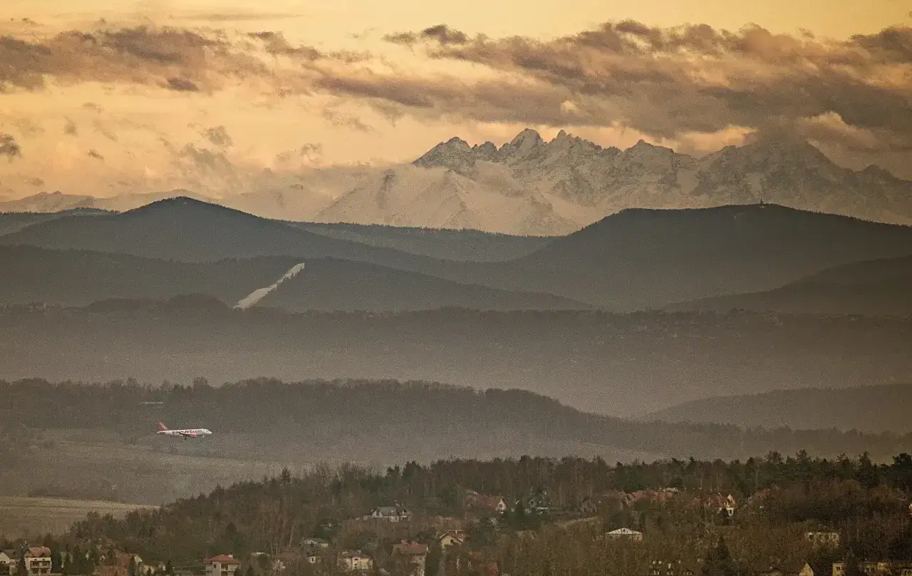 Widok na Tatry z Krakowa. Samolot leci nad mglistymi wzgórzami, a za nimi widać ośnieżone szczyty.