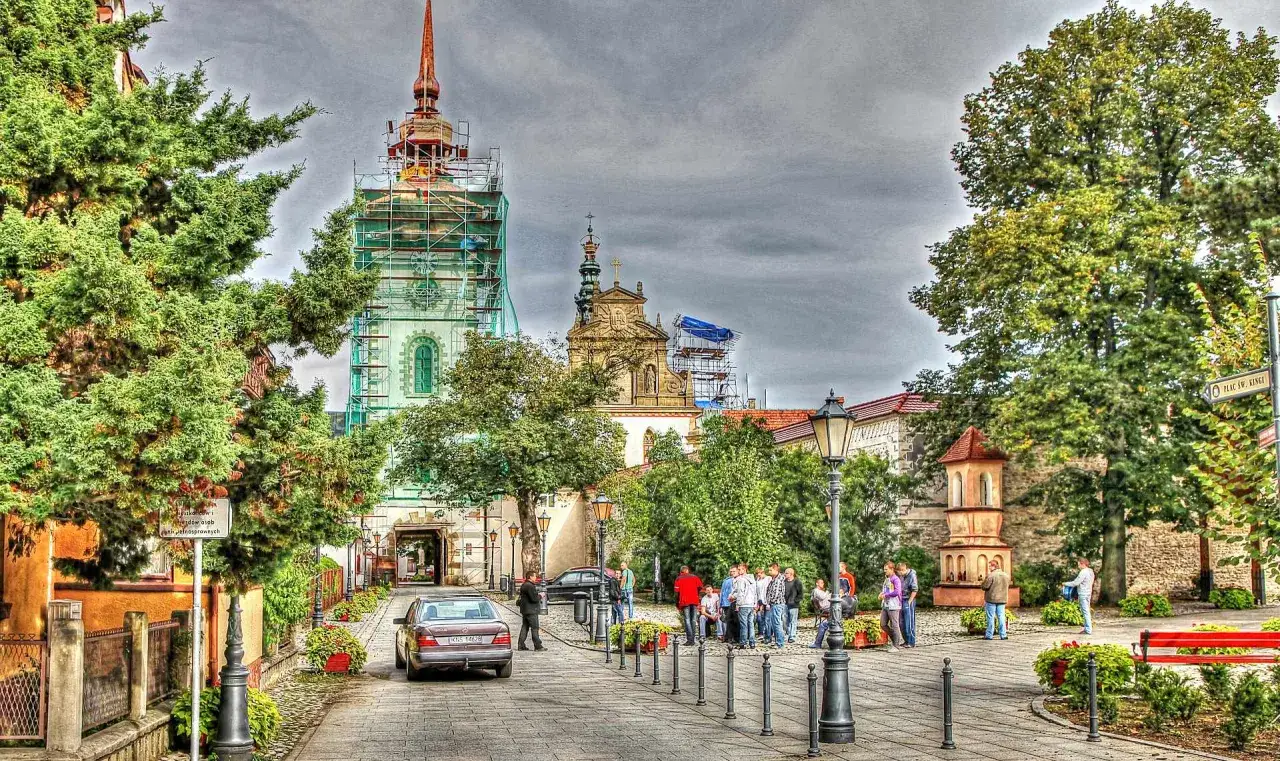 Stary Sącz atrakcje: plac z grupą ludzi, zabytkowe budynki w remoncie, drzewa i brukowana ulica.