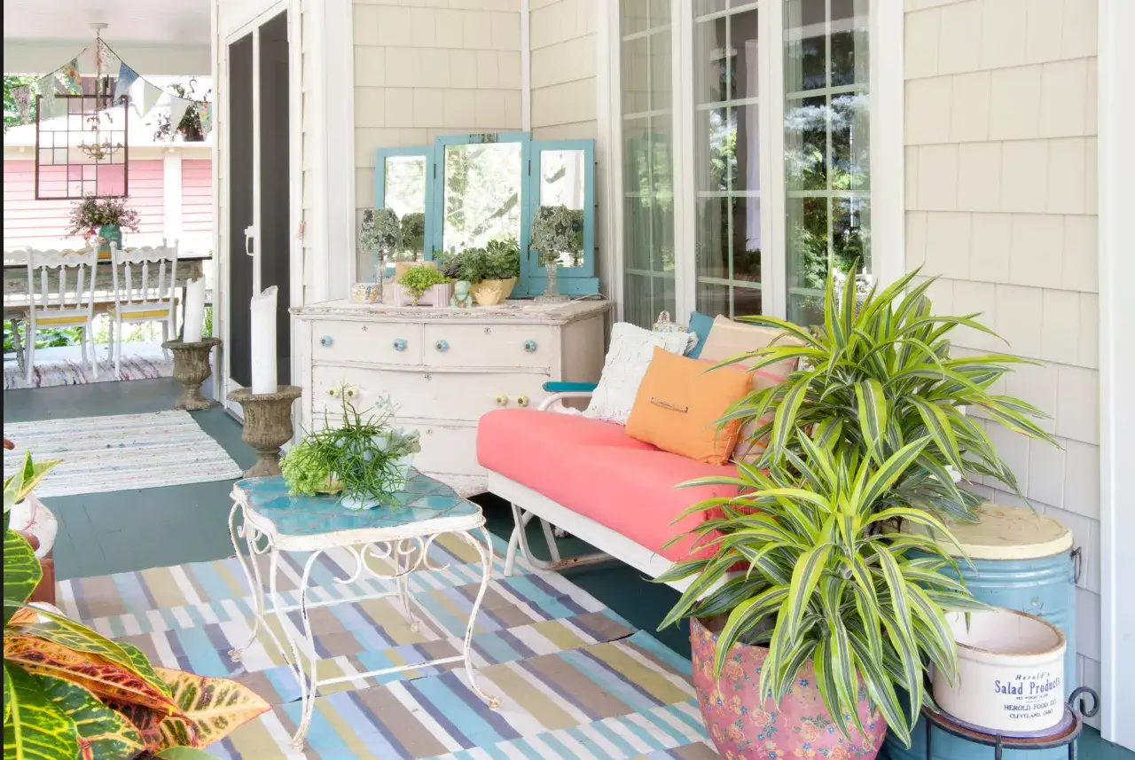Ideas para decorar porche de entrada: un sof&aacute; coral, mesa auxiliar turquesa, plantas y alfombra colorida crean un espacio acogedor.