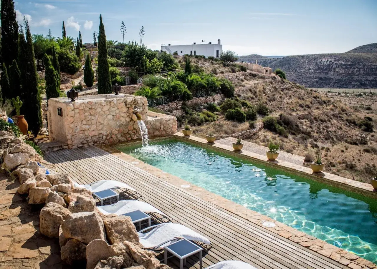 Piscina con cascada en un cortijo de Cabo de Gata. Tumbonas y vegetación mediterránea en un paisaje árido.