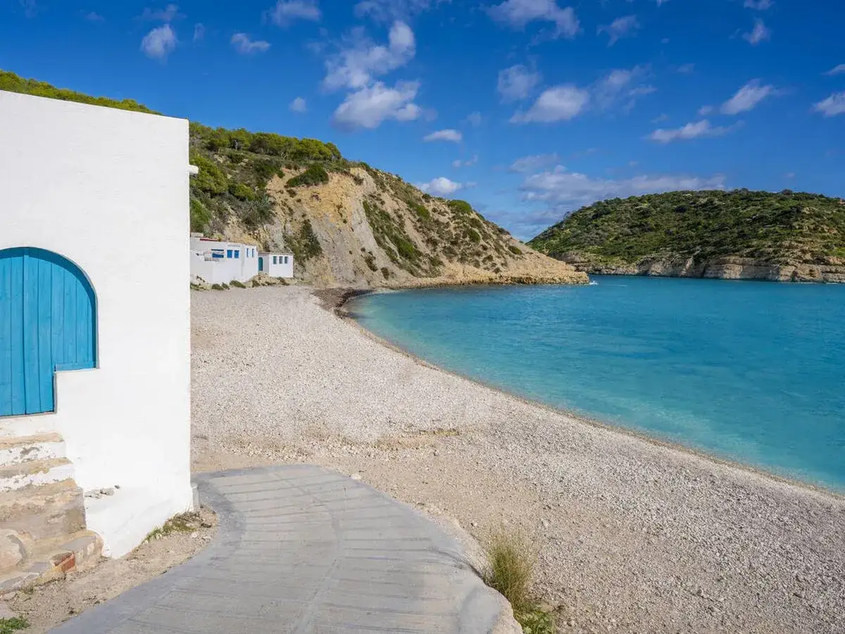 La **cala Barraca** con sus aguas turquesas y casitas blancas, un refugio idílico bajo el sol.