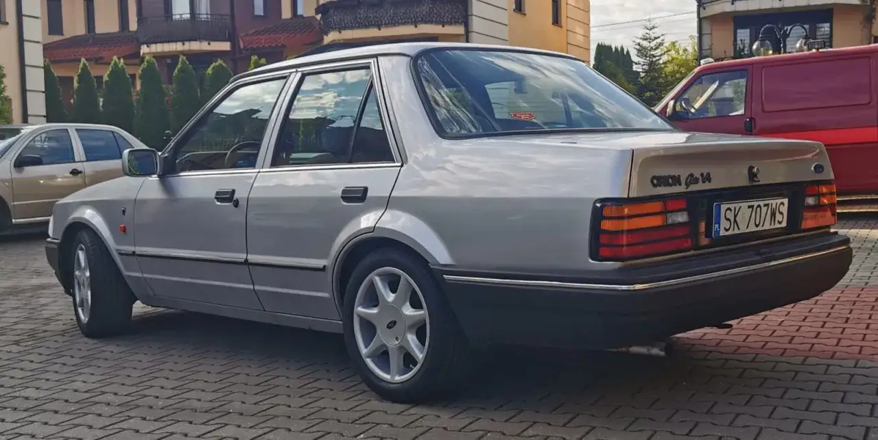 Srebrny Ford Orion z lat 80. na chodniku z kostki brukowej.