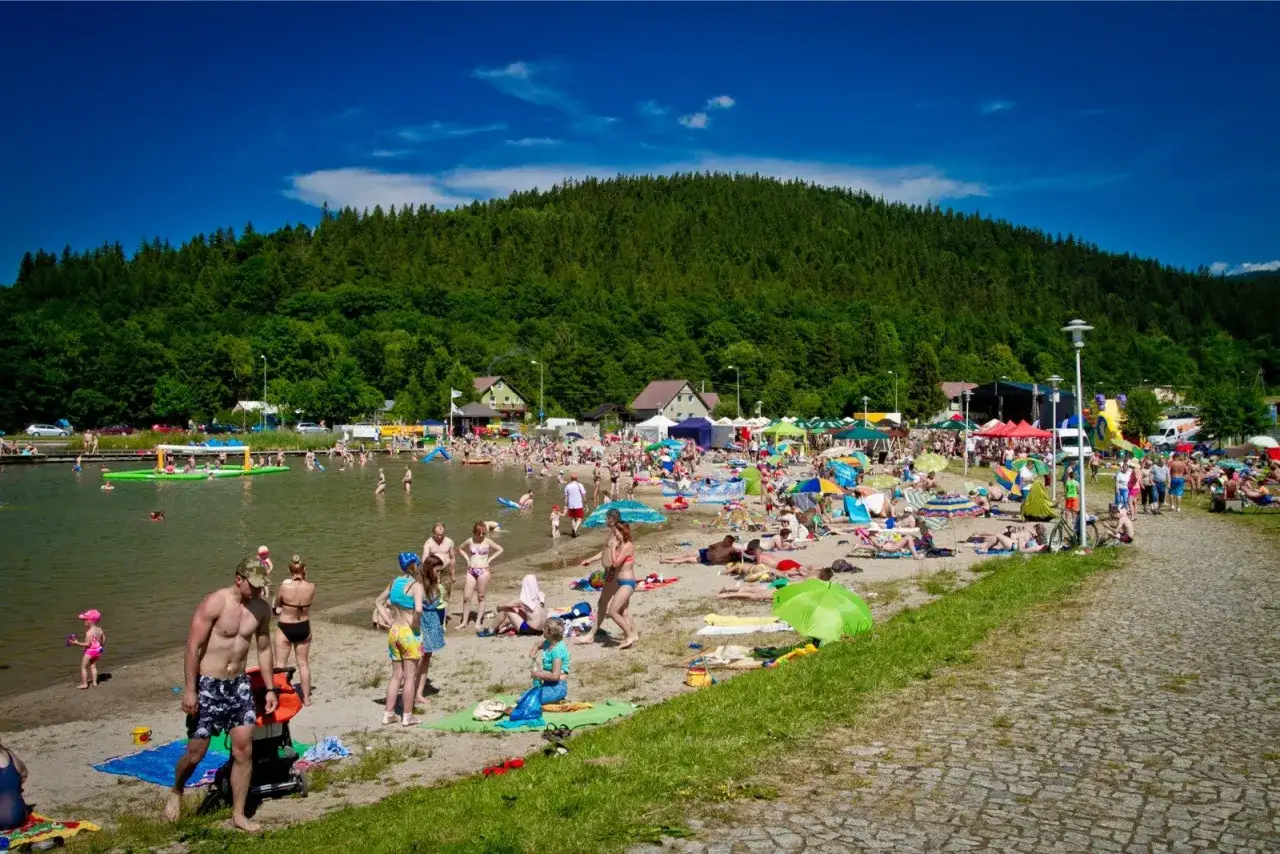 Tłoczna plaża nad jeziorem, ludzie opalają się i kąpią. Idealne miejsce na **dolny śląsk na weekend**.