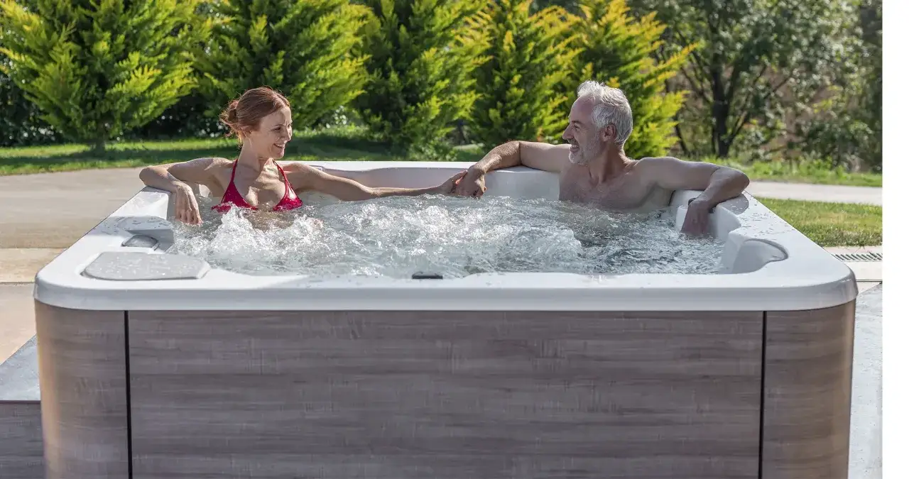 Un couple se tient la main dans un jacuzzi, profitant d'un moment de détente. Ils semblent se demander combien de temps dans un jacuzzi est idéal pour se relaxer.